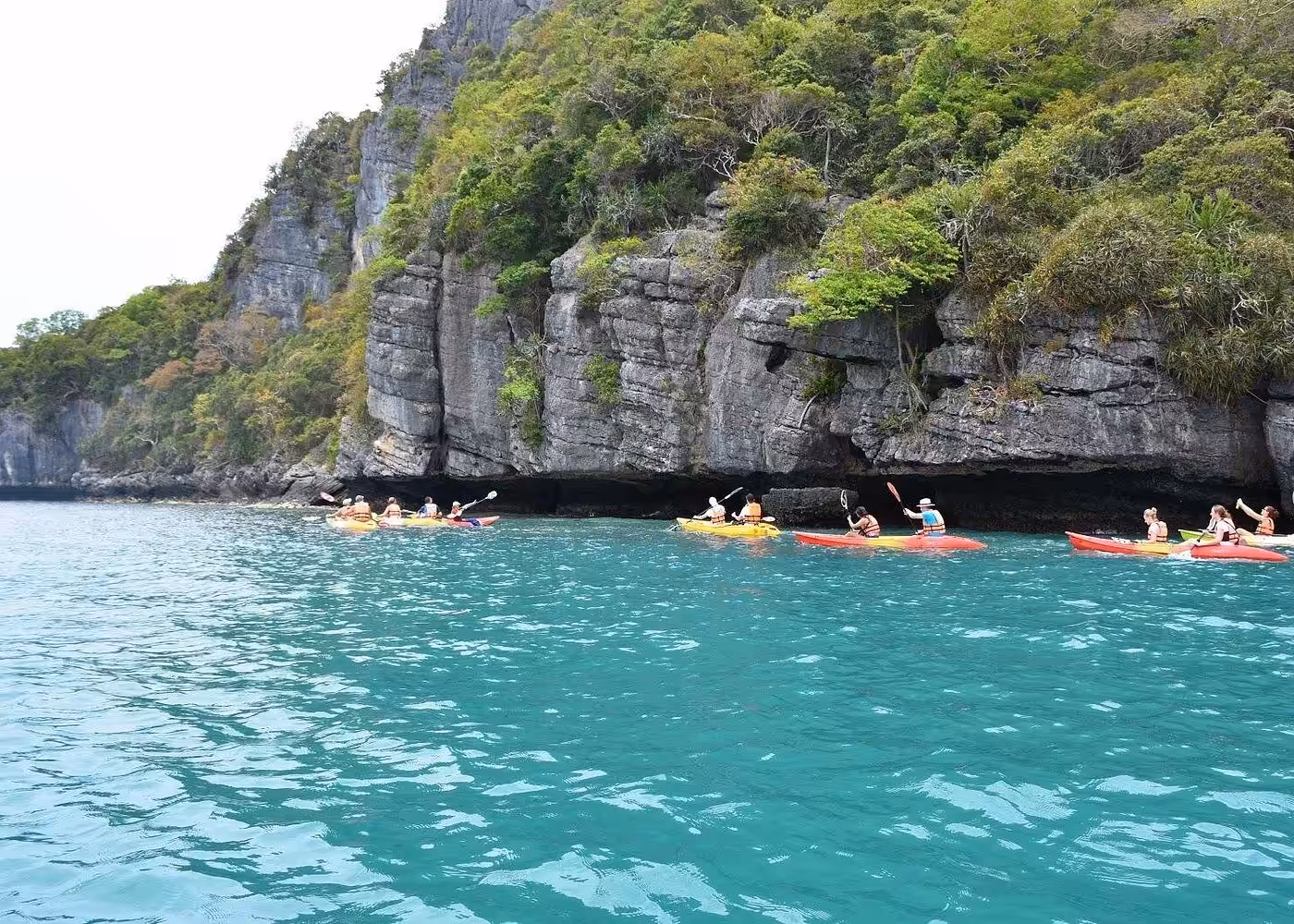 Sea kayaking tour group exploring limestone cliffs and emerald waters in Thailand marine park