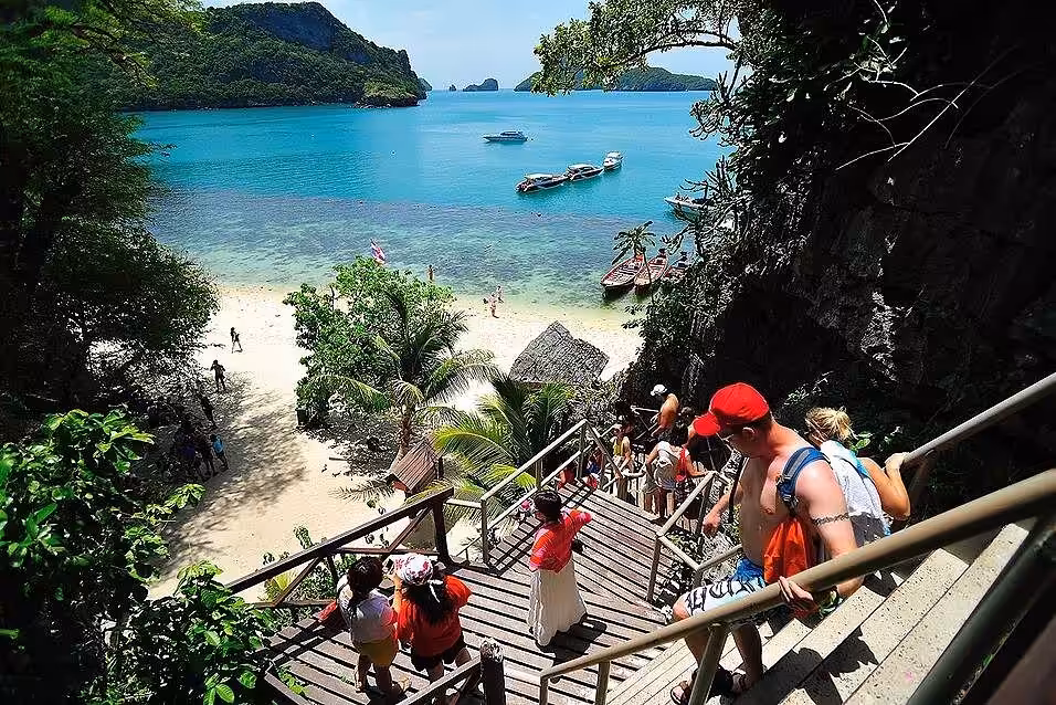 Tourists climbing wooden stairs to viewpoint overlooking pristine beach Wua Ta Lap Island Ang Thong Thailand