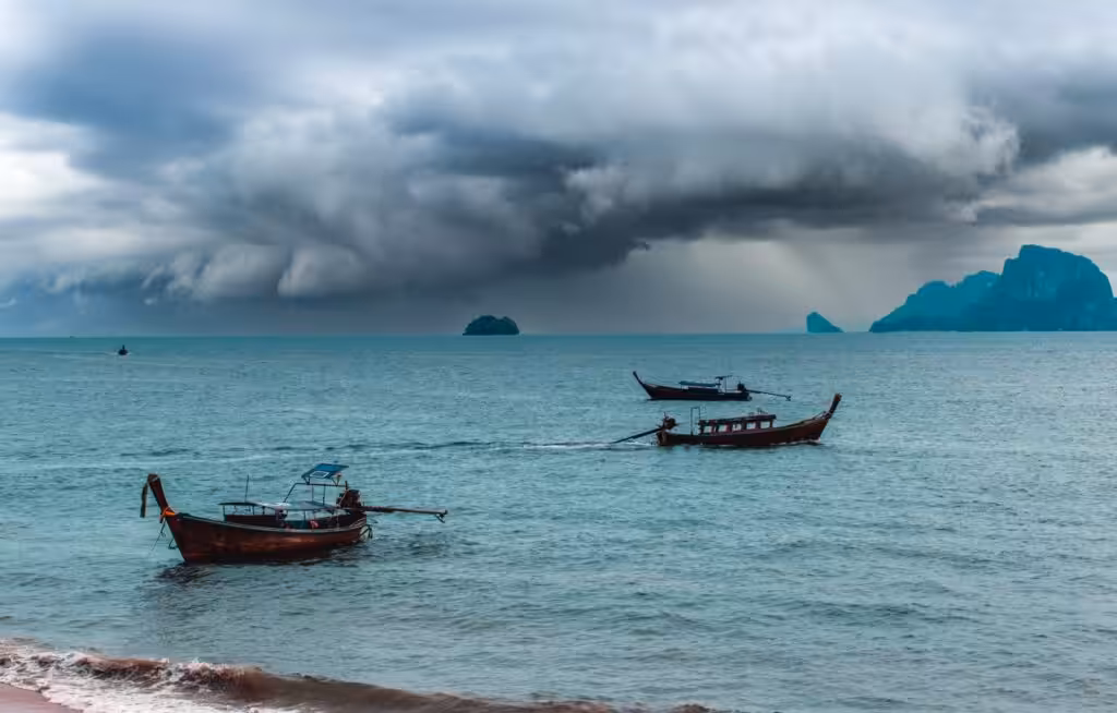 Storm clouds and rain over the Andaman Sea with longtail boats in the foreground during Thailand's rainy season