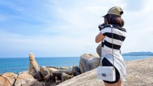 Tourist photographing granite rock formations and ocean views at Koh Samui coastal viewpoint