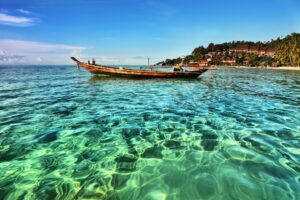 Traditional long-tail boat anchored in crystal clear turquoise waters at Koh Phangan beach, Thailand