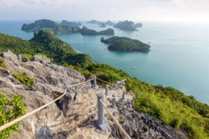 Rocky hillside with a pathway leading down to a serene bay dotted with islands and greenery.