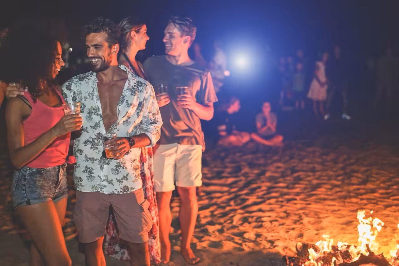 Friends enjoying drinks on the beach at night during a Full Moon Party on Koh Phangan with fire glow in the foreground