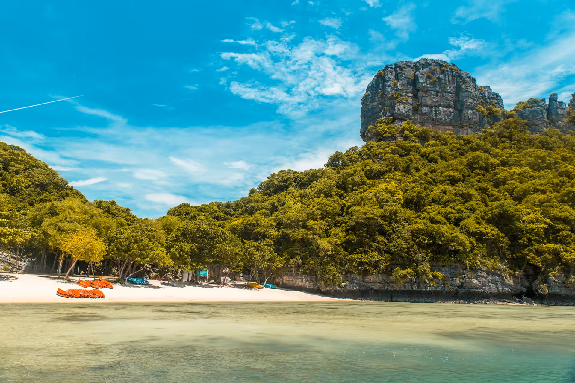 Orange kayaks on a white sand beach beneath a limestone karst cliff in Ang Thong Marine Park, Thailand